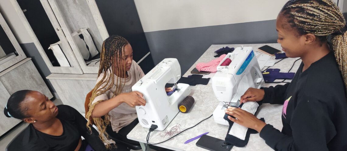 3 Mädchen sitzen an Nähmaschinen und nähen waschbare Binden