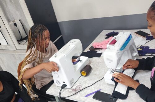 3 Mädchen sitzen an Nähmaschinen und nähen waschbare Binden